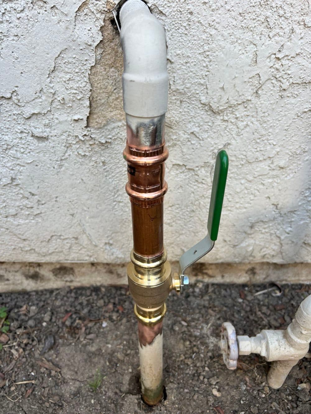 Copper and brass plumbing pipe with valve attached, secured against a textured wall.
