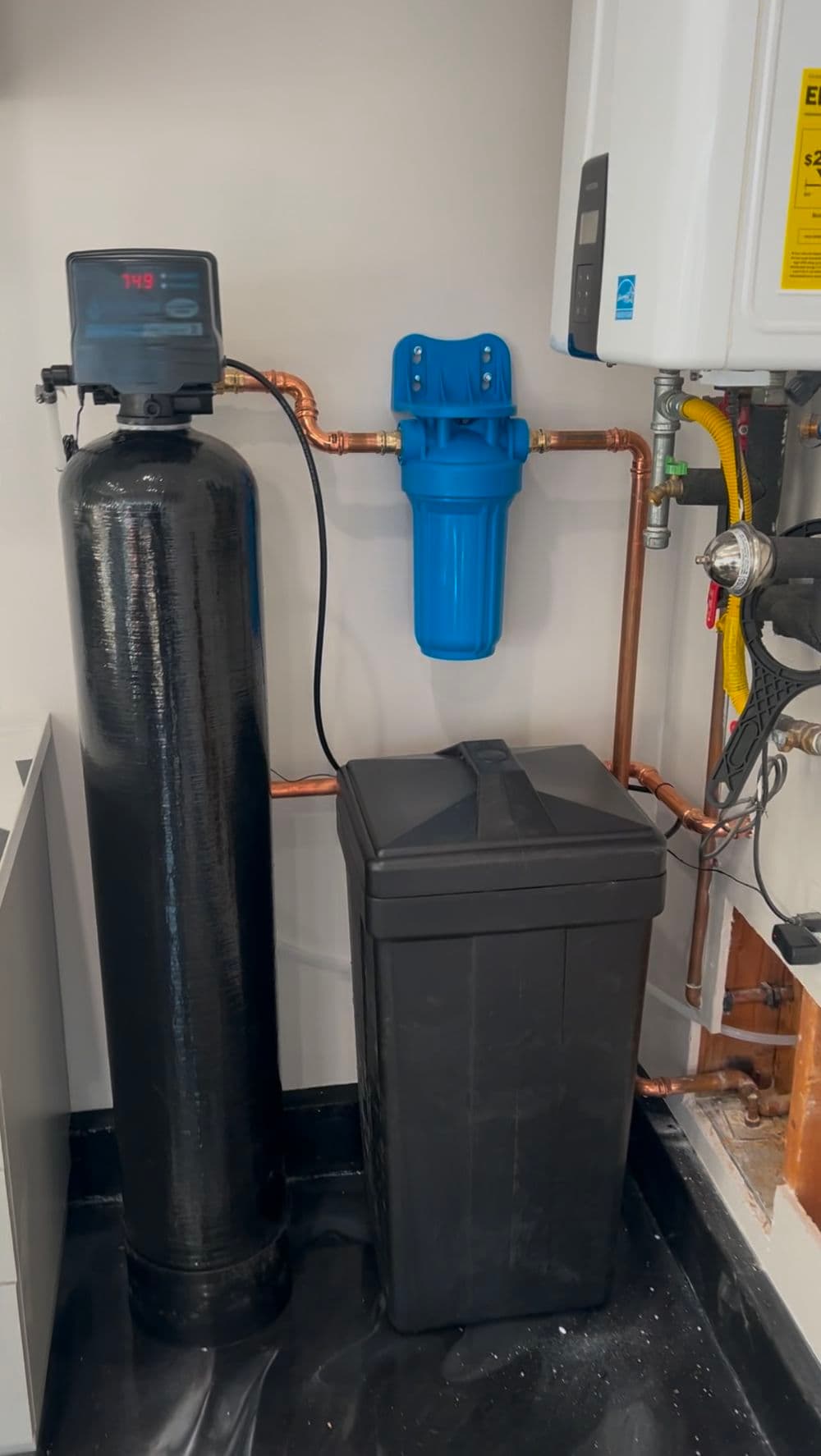 Water filtration system with black tank, blue filter, and copper piping installation.