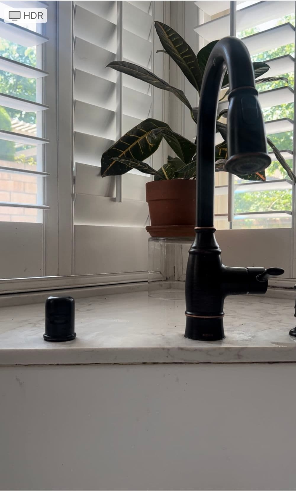 Modern black kitchen faucet with a potted plant in a bright, sunlit window.