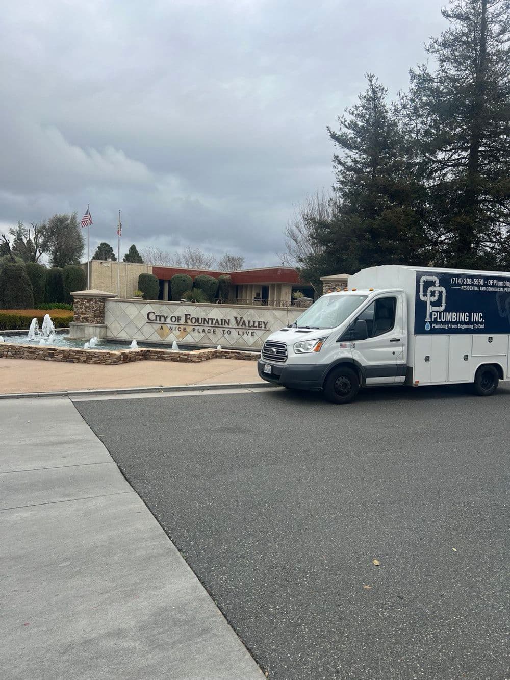 Fountain Valley welcome sign with plumbing van parked in front on a cloudy day.