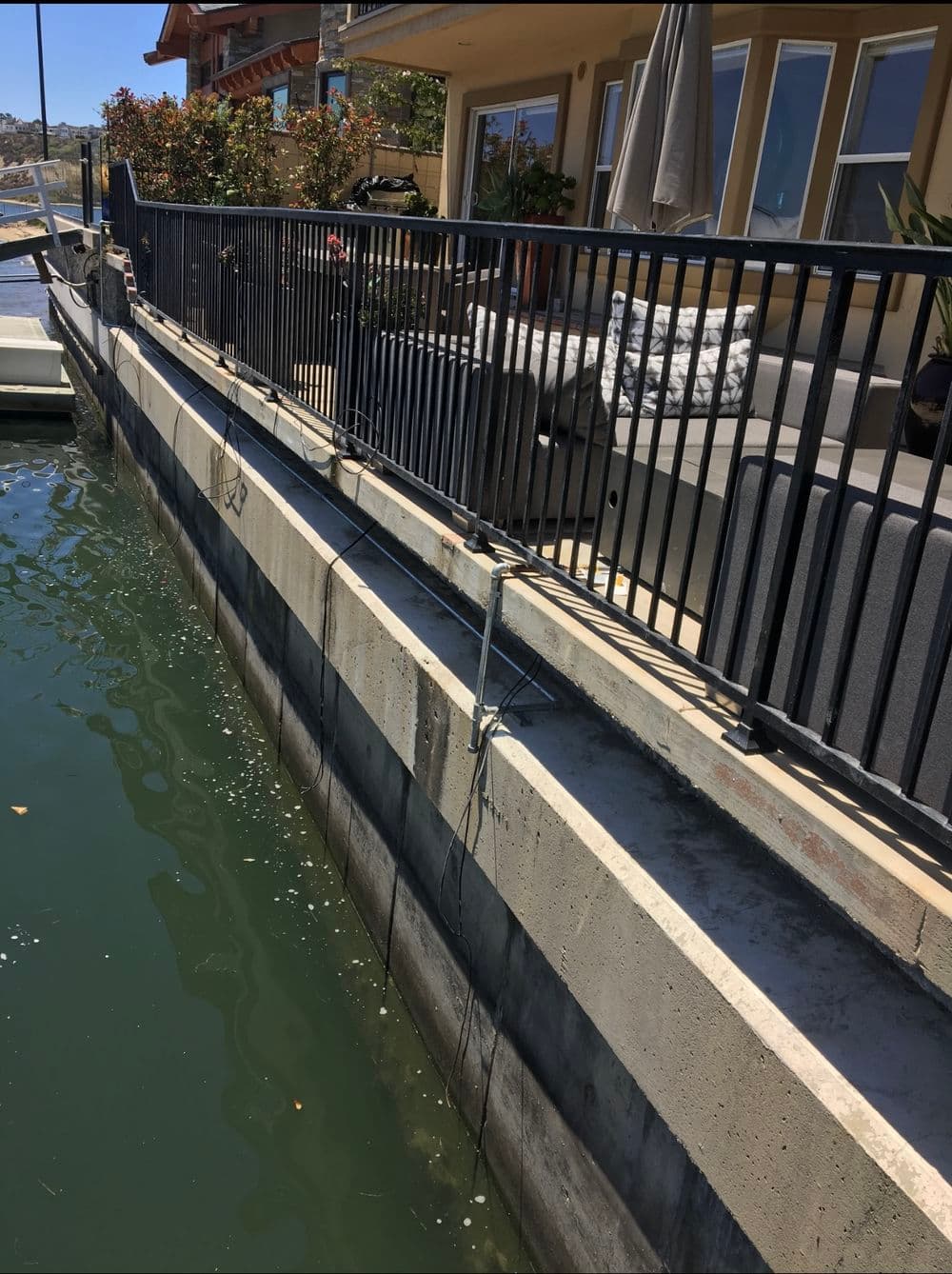 Concrete boat dock with railing, overlooking calm water and nearby residential area.
