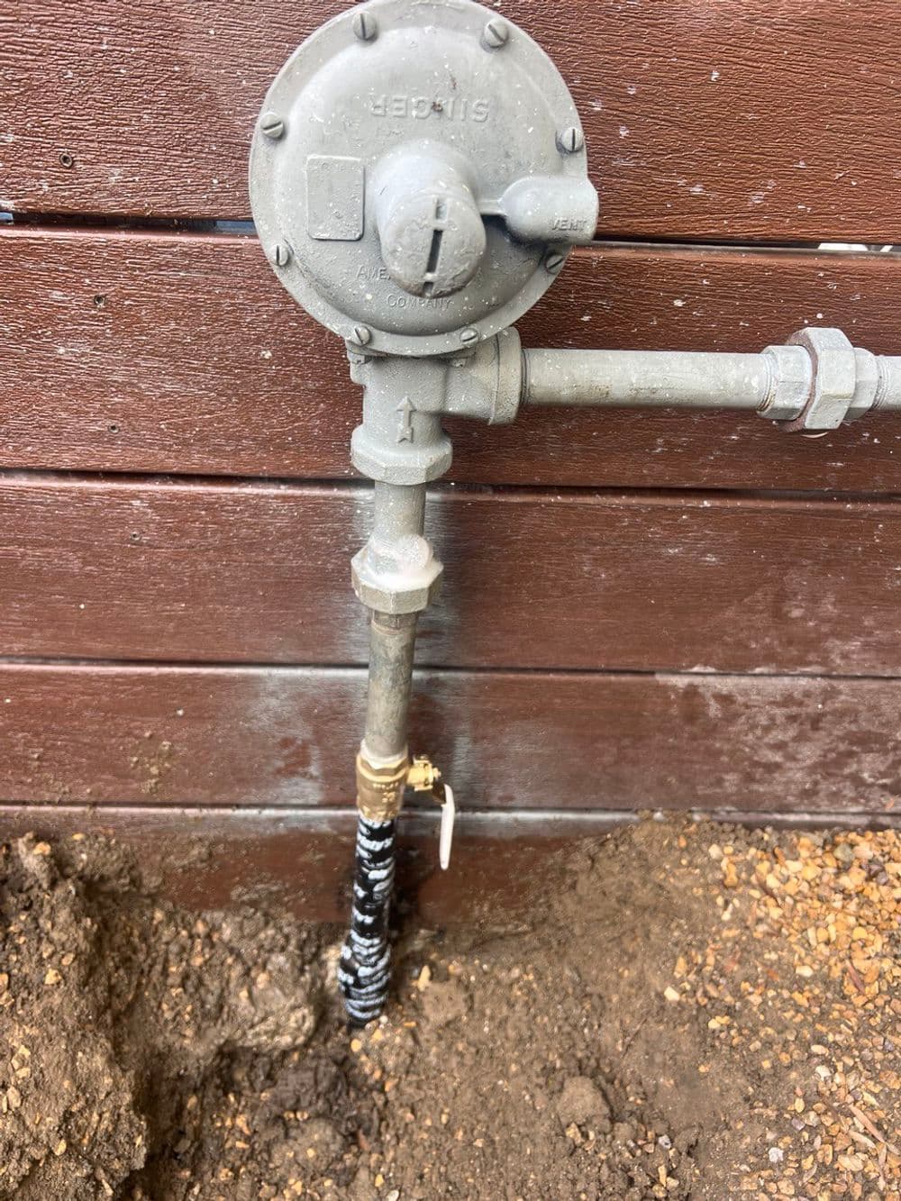 Gas pressure regulator installed on a wooden wall, with connected pipes and tools nearby.