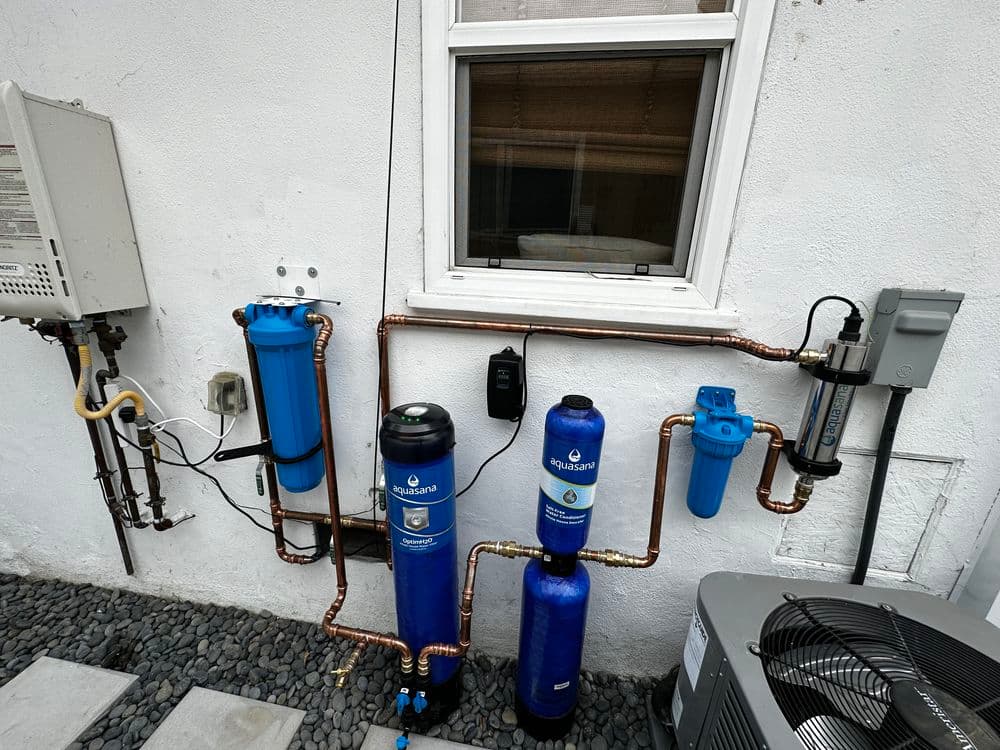 Water filtration system installation with blue canisters and copper pipes on a white wall.