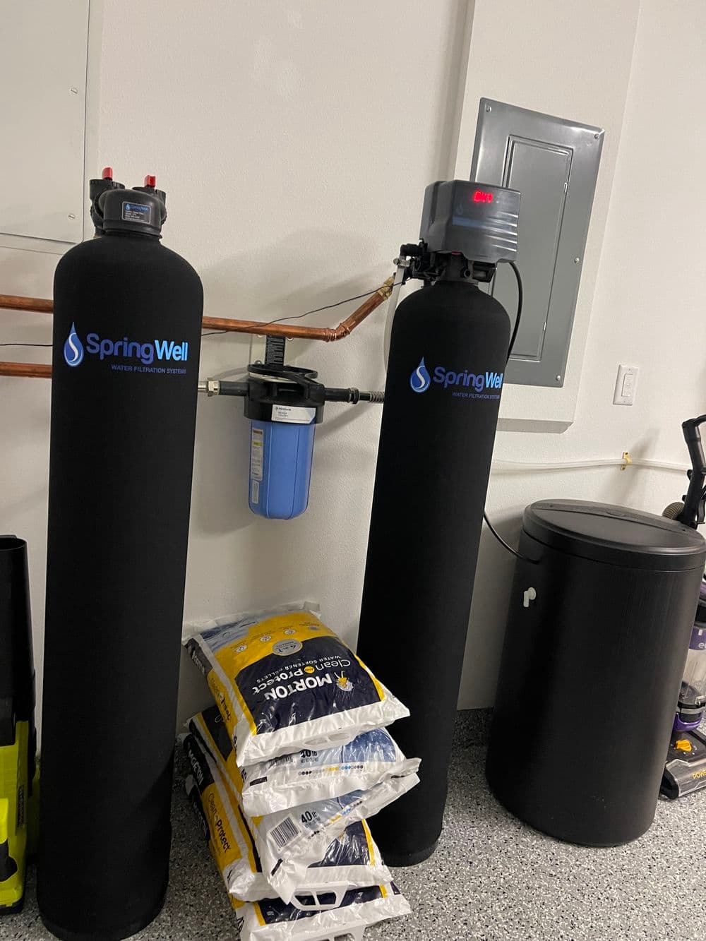 Water filtration system with SpringWell tanks and water softener supplies in a garage setting.