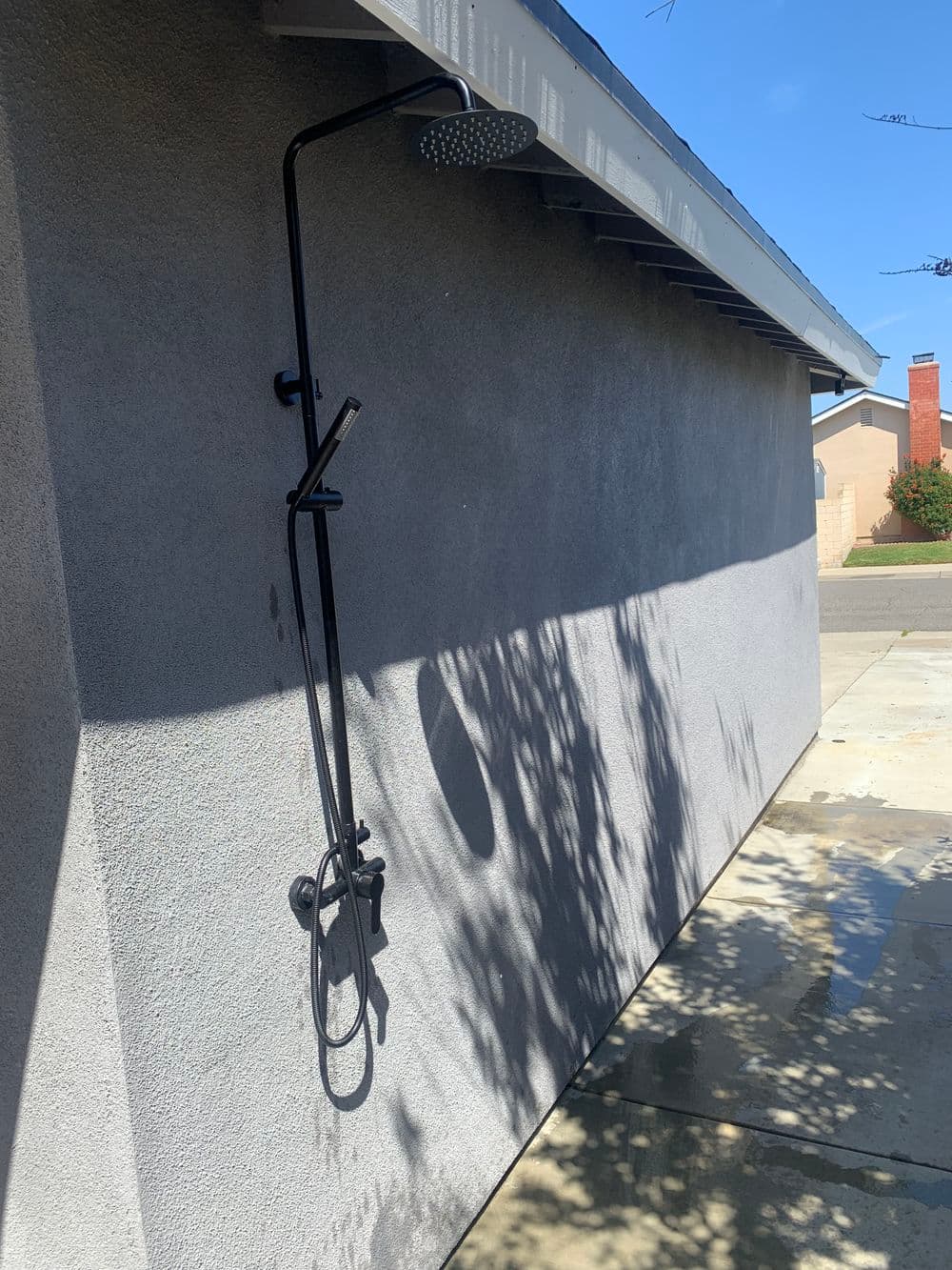 Modern outdoor shower with a black rainfall showerhead against a textured gray wall.