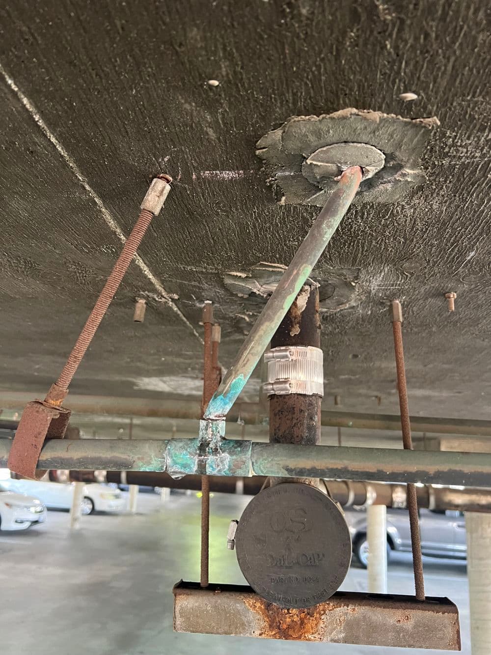 Corroded plumbing in a parking garage showing exposed pipes and rust under a concrete ceiling.