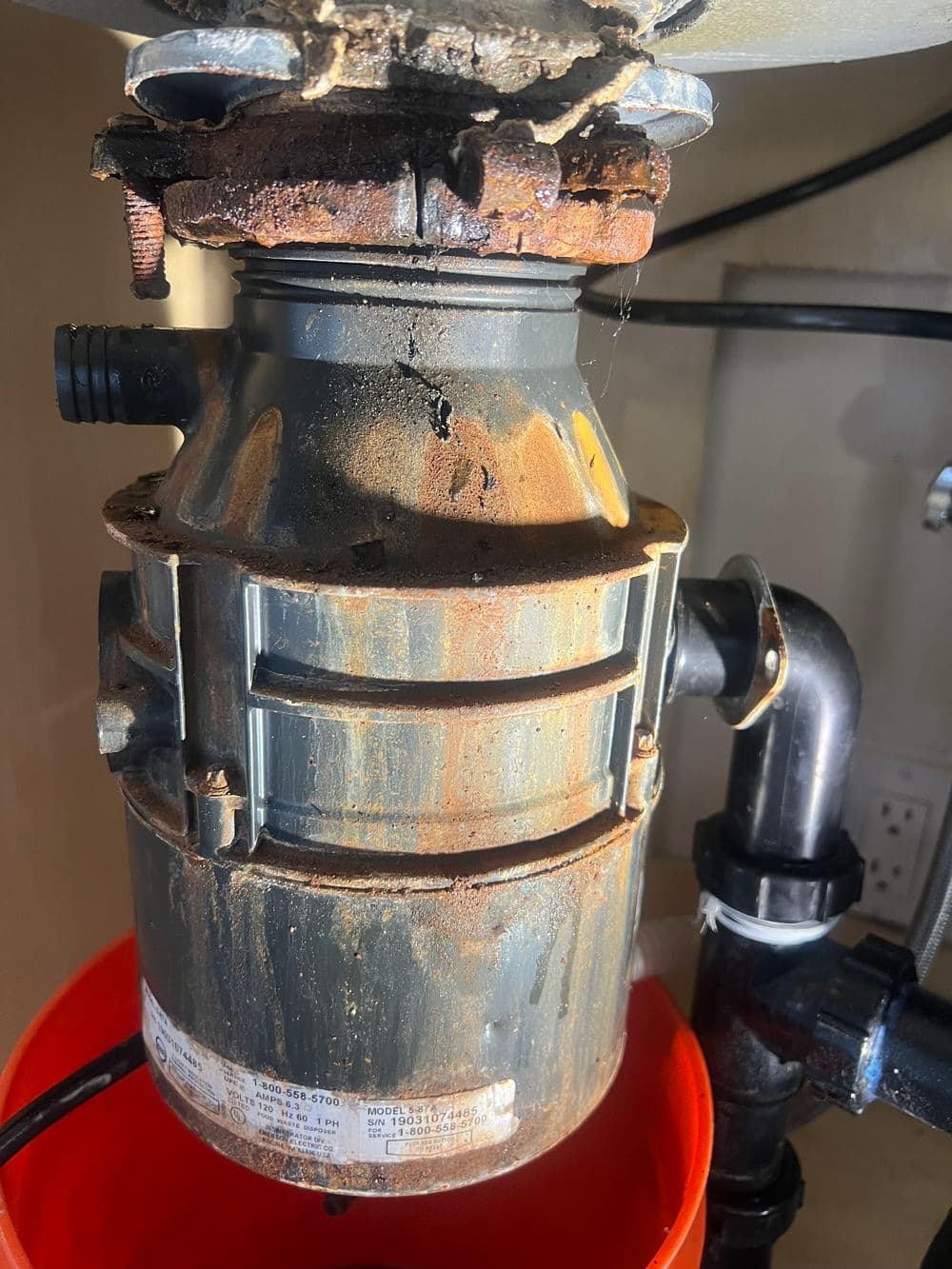 Rusty garbage disposal unit showing signs of wear and maintenance needed, with plumbing connections visible.