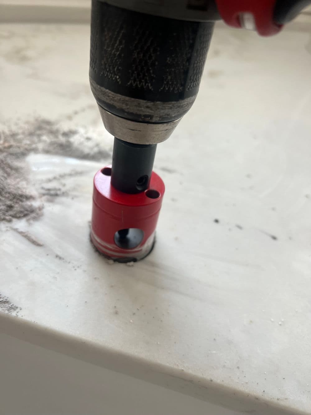 Red drill bit attachment on a white surface with tool markings and dust.