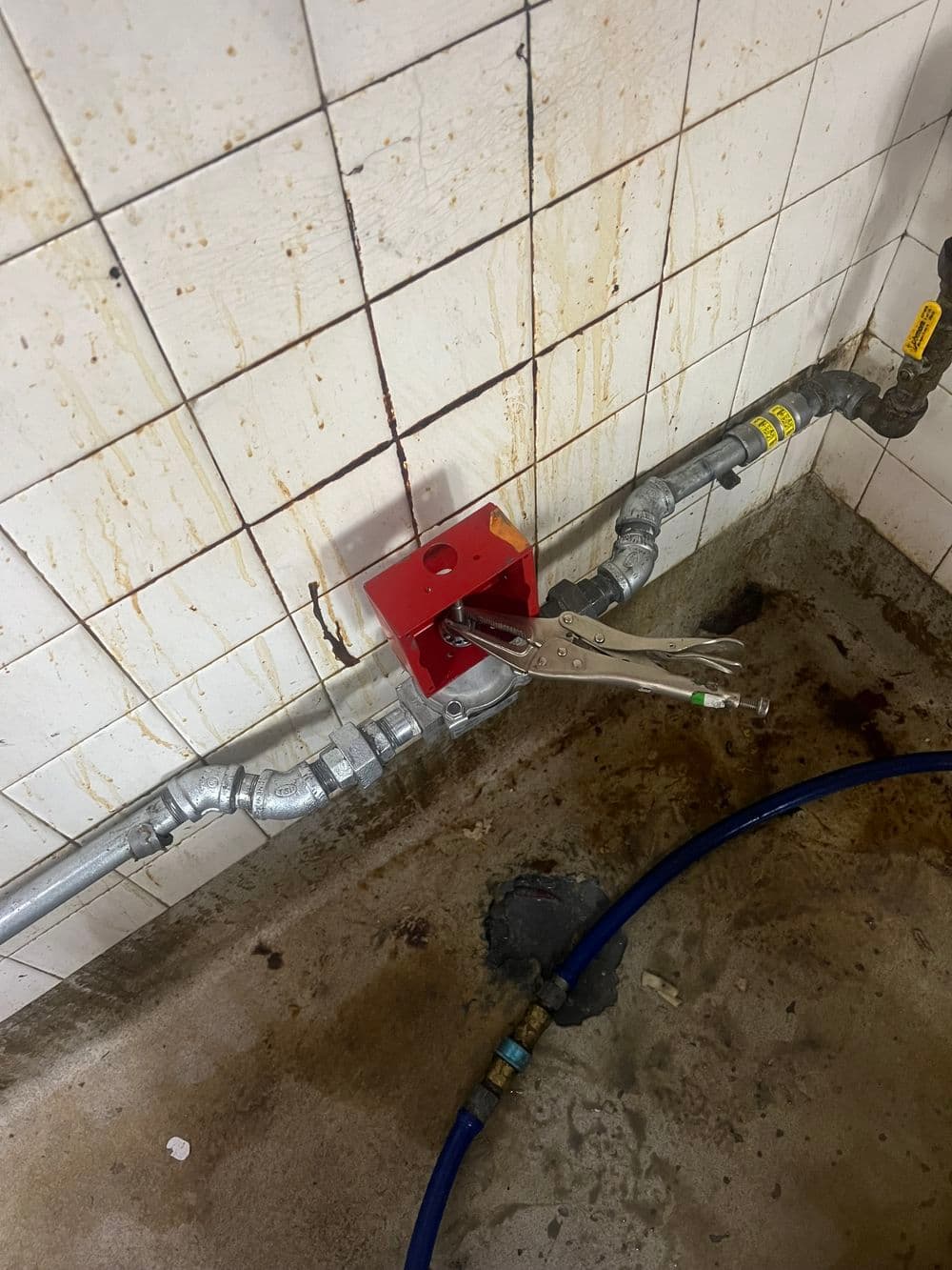 Red valve clamp attached to pipes in a wet floor environment with visible stains.