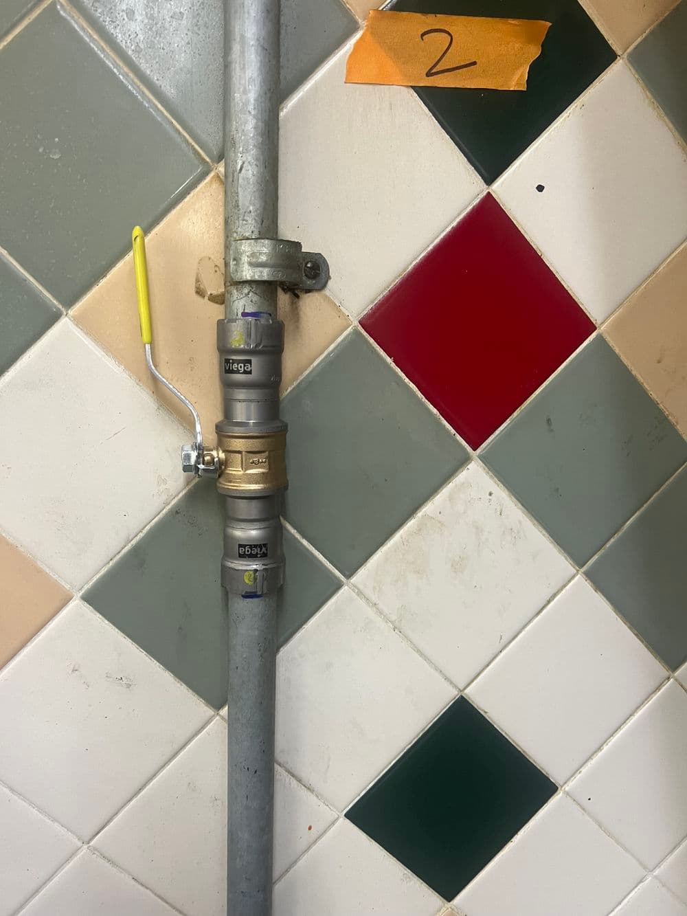 Brass valve and pipe against colorful tiled wall, marked with label "2."