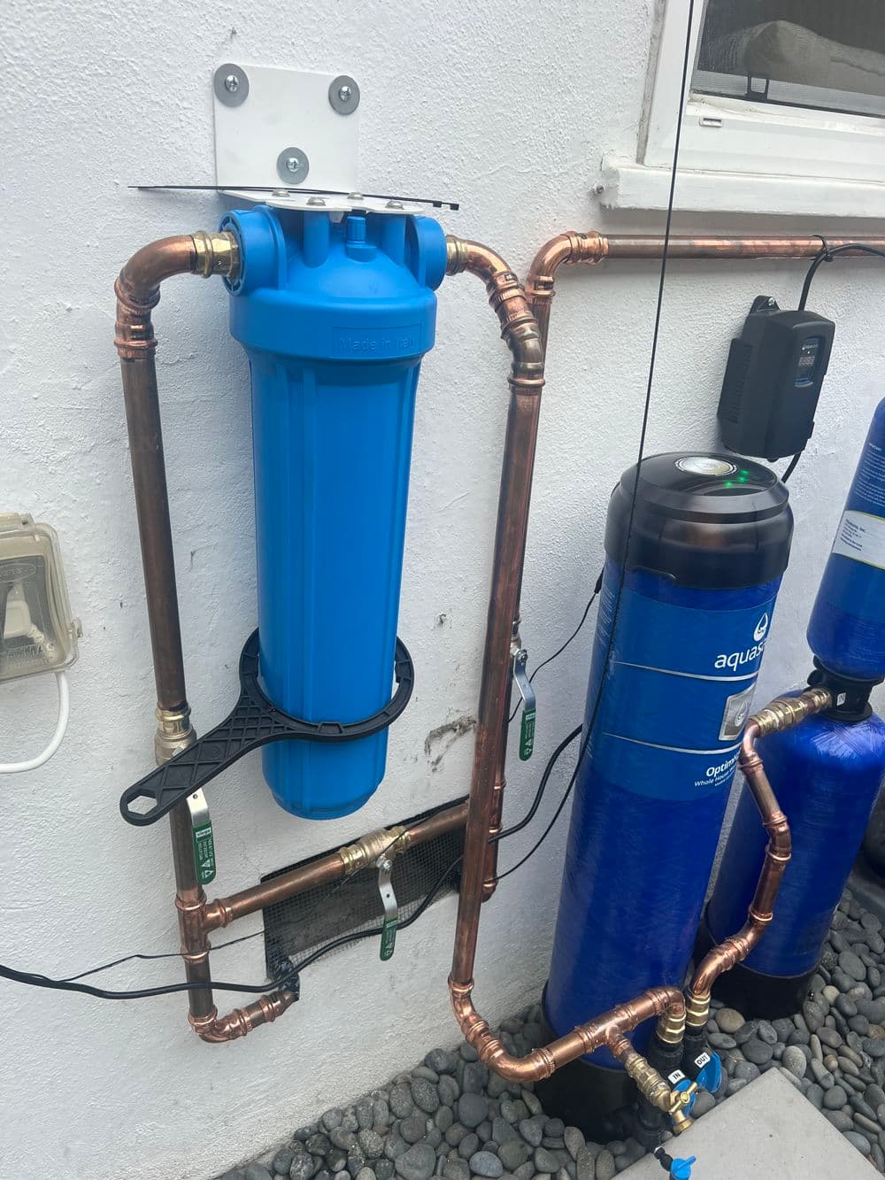 Blue water filter system installed with copper piping and a control panel on a wall.
