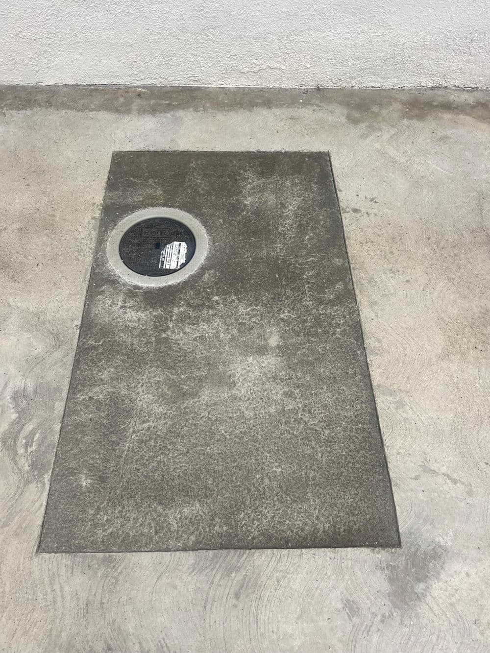 Concrete surface with a round manhole cover in the center, set against a light wall.