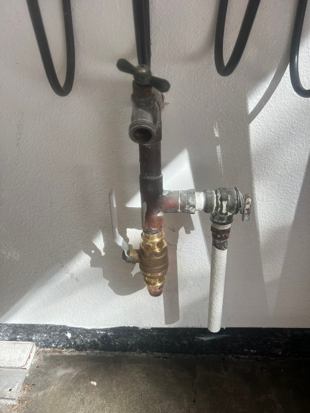 Pipe and valve assembly on wall, featuring brass connection and white water pipe.