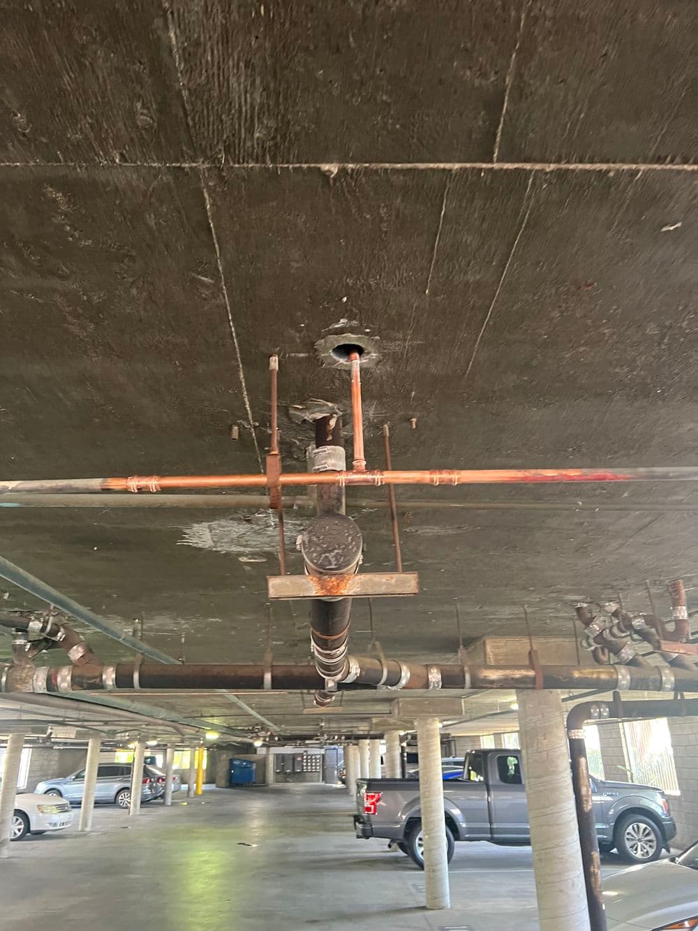 Underside of a parking garage showing rusty pipes and concrete ceiling.